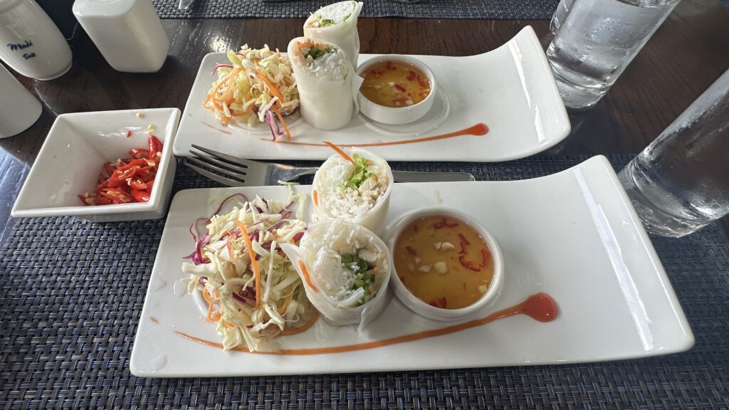 Image of a rice noodle salad wrap with a spicy dip. The wrap is made with rice noodles, vegetables, and protein, and is topped with a spicy sauce.
