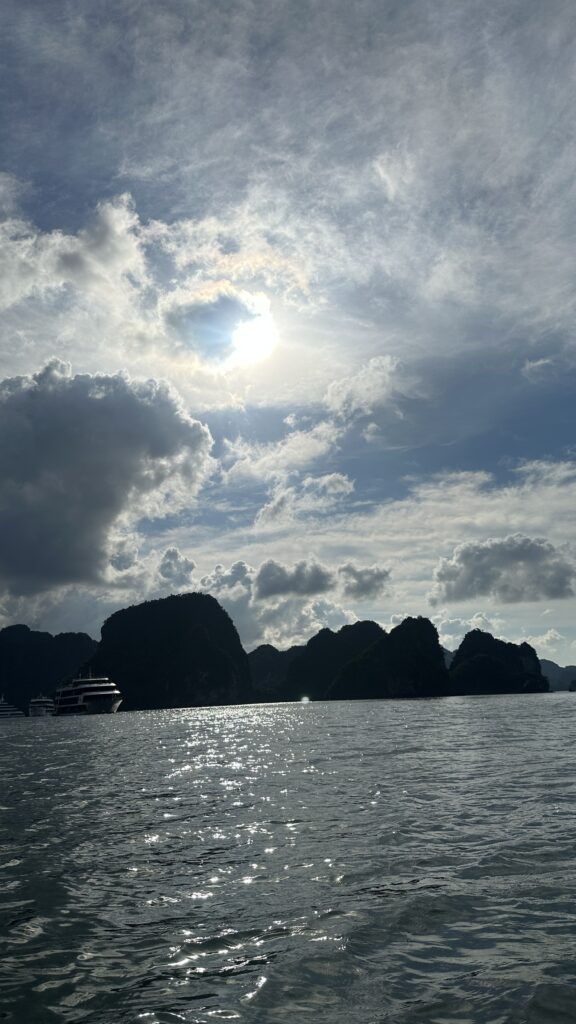 Image of Ha Long Bay, a UNESCO World Heritage Site in Vietnam. The bay is home to thousands of limestone karsts and islands, which rise up from the turquoise waters. The view is taken from a boat, and the sky is blue and the sun is shining.