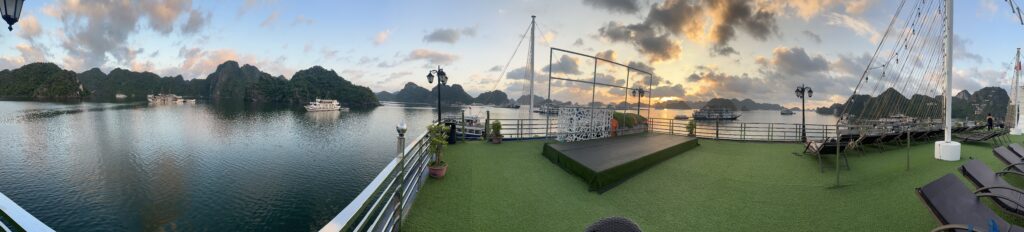 Panoramic view of Ha Long Bay, a UNESCO World Heritage Site in Vietnam. The bay is home to thousands of limestone karsts and islands, which rise up from the turquoise waters. The view is taken from a boat, and the sky is blue and the sun is shining.